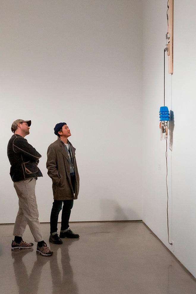 two people examining a tall sculpture hung on the wall